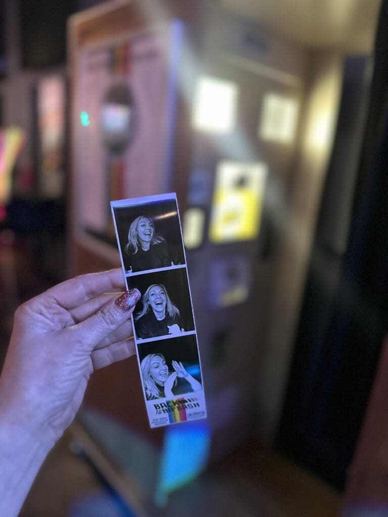Photobooth strip being held in front of a retro photobooth from the early 2000’s mall
